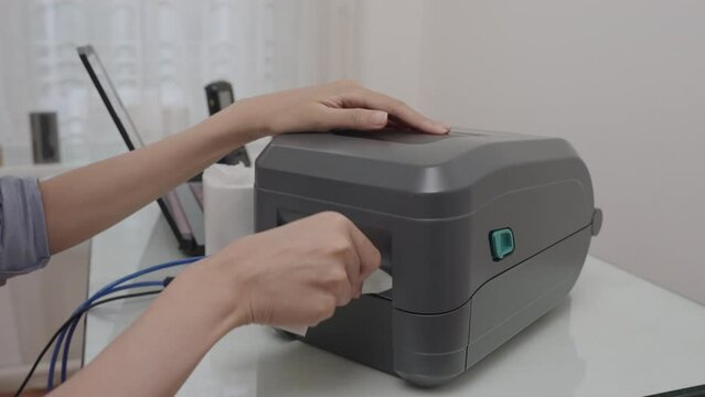Asian beautiful woman use black barcode printer is printing the QR code on the sticker.