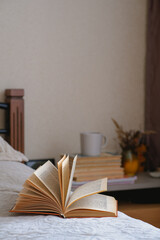 Old open book with yellow pages lies on a beige bed with pillows. Cozy fall mood in a room. Home education. Reading as a hobby. Mental health. Wellbeing, emotional support. Urban life. Indoor interior