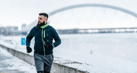 Fototapeta na wymiar Handsome middle age man with a beard running and exercising outside on extremely cold and snowy day. Sport and fitness motivation theme.