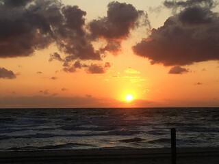 at the sea the red-golden sun shines out from behind the clouds before it sets