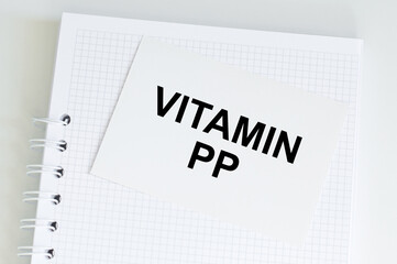 Vitamin PP inscription on a white business card that lies on the page of the notebook on a light table