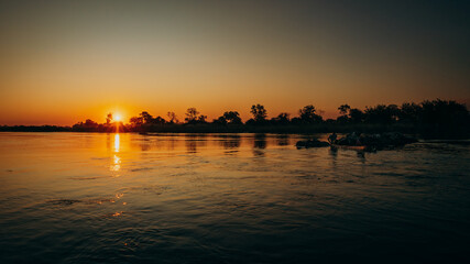 Fototapeta na wymiar Idyllische Sonnenuntergangsszene am Okavango mit Boot-Silhouette (Namibia)
