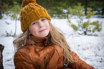 In winter, on a frosty day in the forest, a cute girl stands happy.