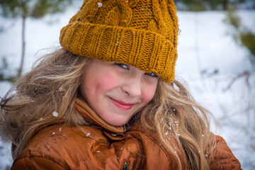 In winter, on a frosty day in the forest, a cute girl stands happy.