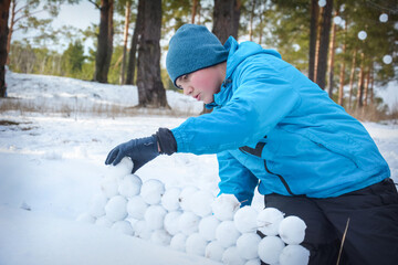 In winter, a boy plays in the forest, he makes snowballs and builds a fortress out of them.