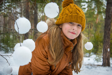 In the winter afternoon in the forest, a girl makes snowballs with a snowball and decorates tree branches.