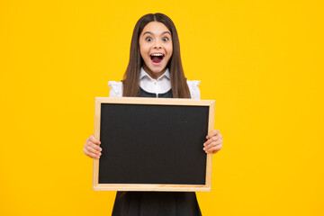 Teenager child holding blank chalkboard for message Isolated on a yellow background. Empty text blackboard, copy space mock up. Excited face, cheerful emotions of teenager girl.