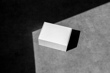 Blank white paper box, packaging mockup, on concrete background, with sharp natural sunlit shadows....