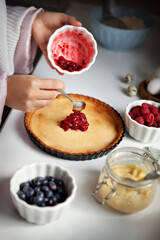 Closeup woman hands cooks cake with raspberries. Woman prepares at kitchen