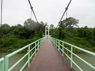 Fototapeta na wymiar The green light handrail with a brown walkway and white suspension bridge at Sirindhorn District, Ubon Ratchathani Province, Thailand.