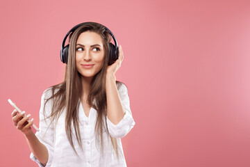Beautiful woman listening to music using wireless headphones in studio isolated over pink background.Girl uses wireless earphones and dancing.