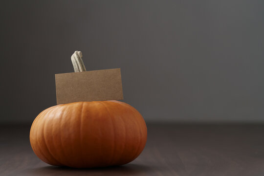 Small orange pumpkin on walnut wood table with copy space and empty paper card