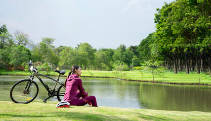 side view asian transgender in sportswear sitting beside the pond with bicycle after cycling,...
