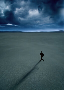 Man in black suit runs in desert with a blue cloudy sky. High angle view. 3D render.