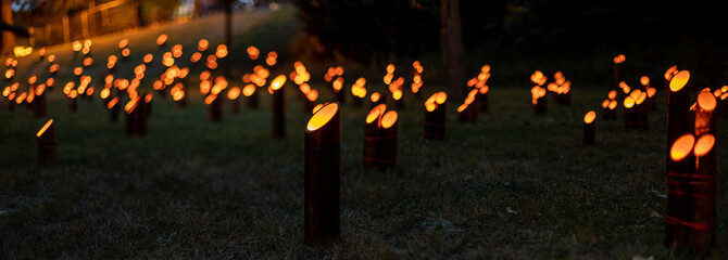 Hundreds of Japanese bamboo lanterns - candles in bamboo stands - flickeringly illuminate the dark,...