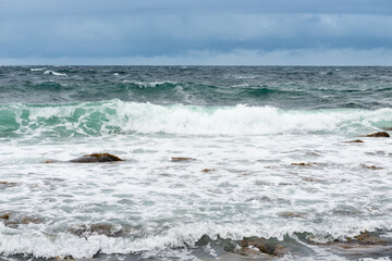 Dangerous sea wave crashes on a rocky coastline with splashes and foam before a storm in the Barents Sea