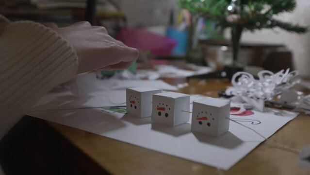 Girl strings paper crafts in shape of snowman on thread. Concept of decorating room before Christmas.