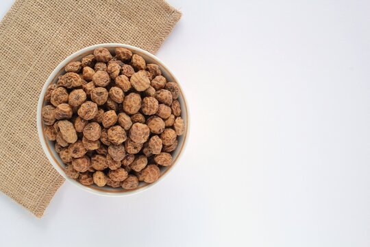 Chufa, tigernut, earth almond on white ceramic bowl and eco canvas bag on white background. Healthy vegan food concept. Tiger nut for flour, oil, milk, traditional drink horchata. Copy space for text