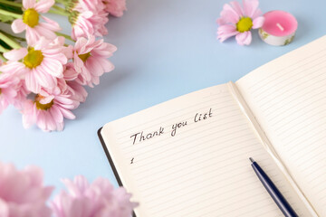 Handwritten words Thank you list in a personal diary on a light blue background with pink flowers. Gratitude journal concept