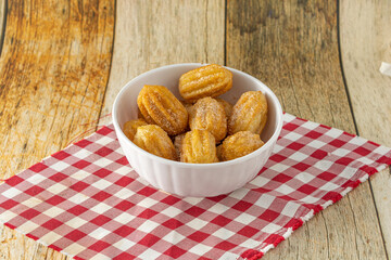 brazilian mini churros, a traditional snack for party with sugar and cinnamon powder in a white container and wooden background