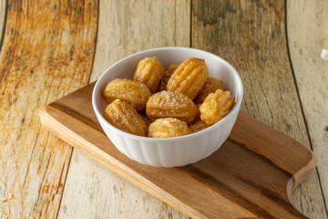 brazilian mini churros, a traditional snack for party with sugar and cinnamon powder in a white container and wooden background