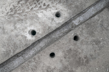 A trench in the pavement in concrete for a cable and 4 holes for anchor bolts, top view.