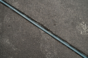 A trench on the pavement in asphalt with a cable, top view.