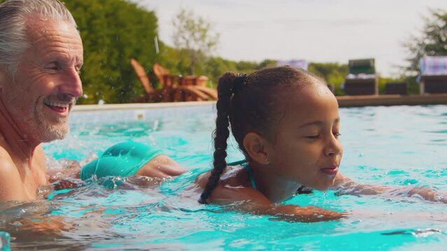 Parents teaching daughter to swim in outdoor pool on family summer holiday - shot in slow motion
