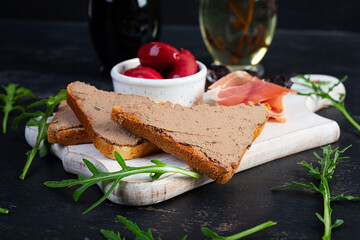 Grilled sandwich with pate with chicken liver and olives on dark background