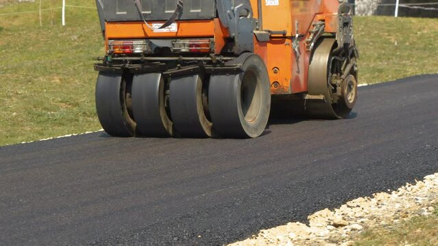 Compacting and smoothing freshly laid road surface with asphalt roller machine. Operating construction machinery while finishing asphalting inclined driveway with bend in beautiful morning light.