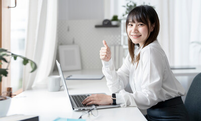 Young Asian businesswoman working on laptop and raised thumb up motivate herself with confident