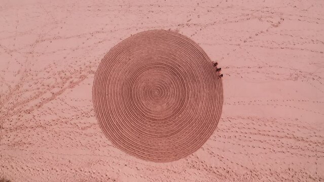 Static aerial top view of people trampling down mysterious spiral circus on sand. Fake mystery and sports exercise for tourists on seaside. Rite with ancient symbol. Enigmatic sign on sandy beach.