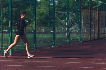 Fototapeta premium Morning run at the stadium. The girl with the phone goes in for sports.