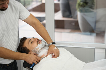 Young gentleman having beard shaved and groomed at local barbershop