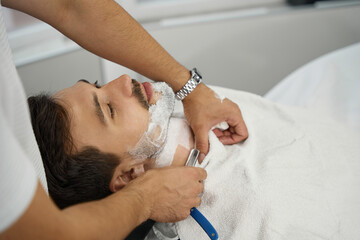 Tranquil gentleman having his facial hair tended to at barbershop