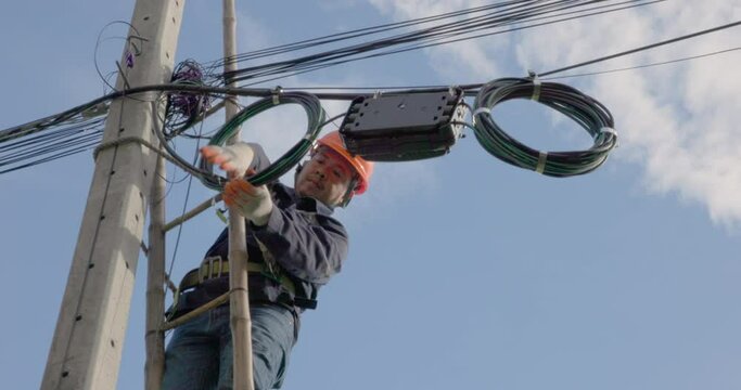 A telecoms worker is shown working from a utility pole ladder while wearing high visibility personal safety clothing, PPE, and a hard hat.