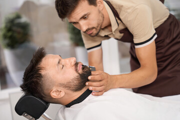 Fototapeta premium Professional barber doing his best while grooming hair of client