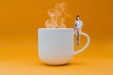 Huge Cup of hot coffee and woman sitting on mug handle and drinking coffee isolated on yellow background. Creative idea for coffee time