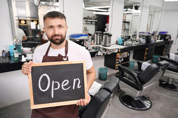 Young hair-grooming professional looking inviting with opening sign in hands