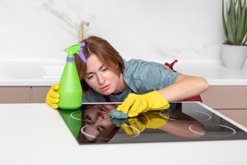 Young attractive housewife in red apron and yellow rubber gloves cleaning stove with rag. Household and cleaning service concept