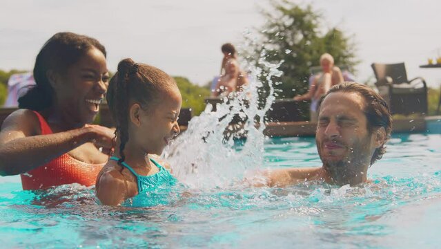 Parents and daughter splashing in outdoor swimming pool on family summer holiday - shot in slow motion