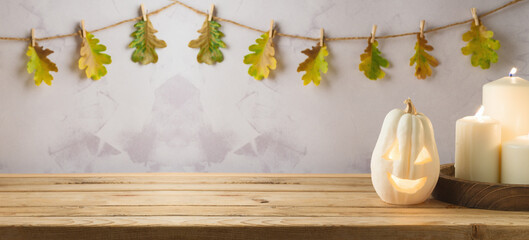 Wooden table with jack o lantern pumpkin and candles over autumn leaves garland background....