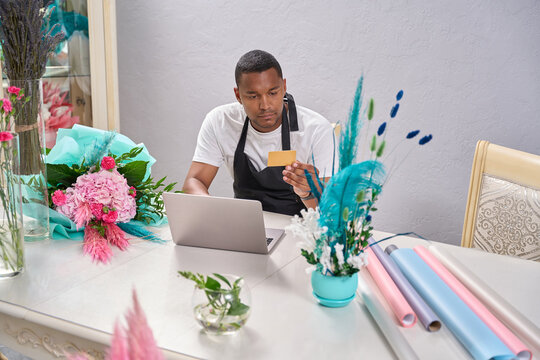 Florist Sits At A Table With A Laptop And Looks At A Small Piece Of Paper