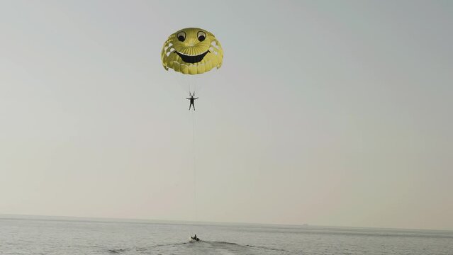 Behind the boat on a parachute - a smiley face a man flies over the sea. Parasailing. Extreme summer fun.