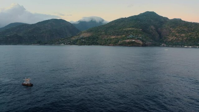Beautiful seascape with an artificial island for mooring ships in coastal waters against background of coast with mountains and thick light clouds. Aerial view of a tropical island in morning.