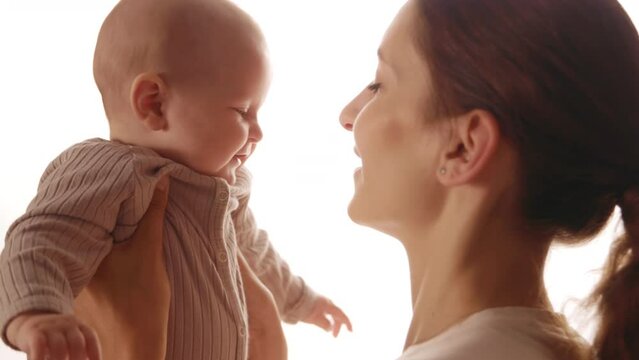 Close up face charming young happy mother is keeping in arms and caressing newborn baby. Smiling. Standing in apartment. Motherhood. Portrait. Slow motion