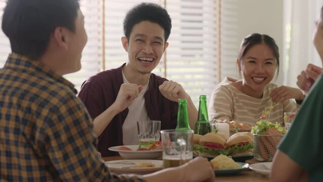 Happy hour good warm summer time diner indoor home. Group of asia people young adult friend man and woman sit at dining table joy fun talk or eat food and drink beer alcohol bottle glass inside house.