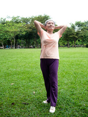 Portrait of senior adult elderly asian woman 60s smiling standing and stretch her arms relax and enjoy with nature fresh air in the park.