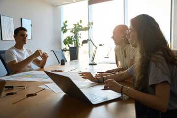 Two female employees look at colleague at desk in office