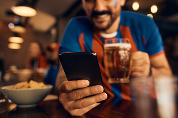 Close up of sports fan using cell phone in bar.